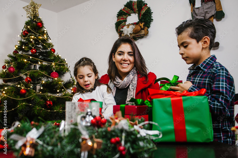 Latin siblings at Christmas with red and green gifts and a decorated fir tree in Mexico Latin siblings at Christmas with red and green gifts and a decorated fir tree in Mexico