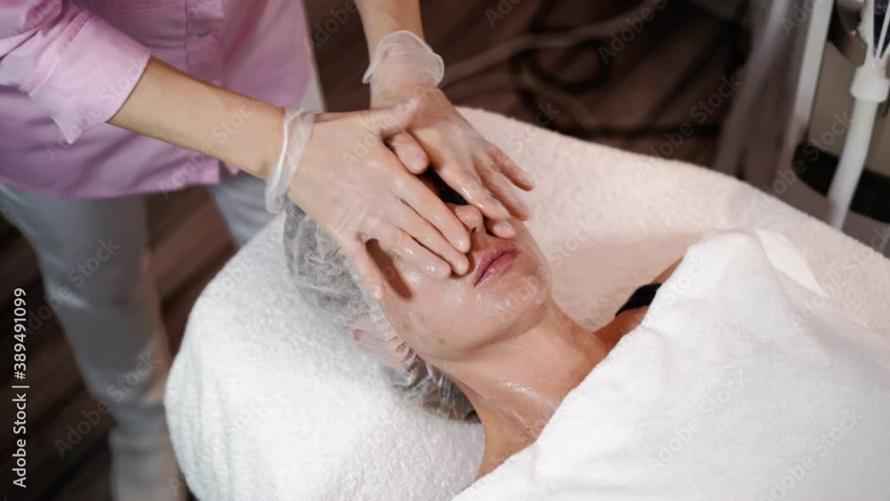 Female beautician prepares for laser rejuvenation and facial hair removal of woman lying on medical couch in beauty salon. Cosmitology, epilation and spa concept. Body and skin care. Close-up Female beautician prepares for laser rejuvenation and facial hair removal of woman lying on medical couch in beauty salon. Cosmitology, epilation and spa concept. Body and skin care. Close-up