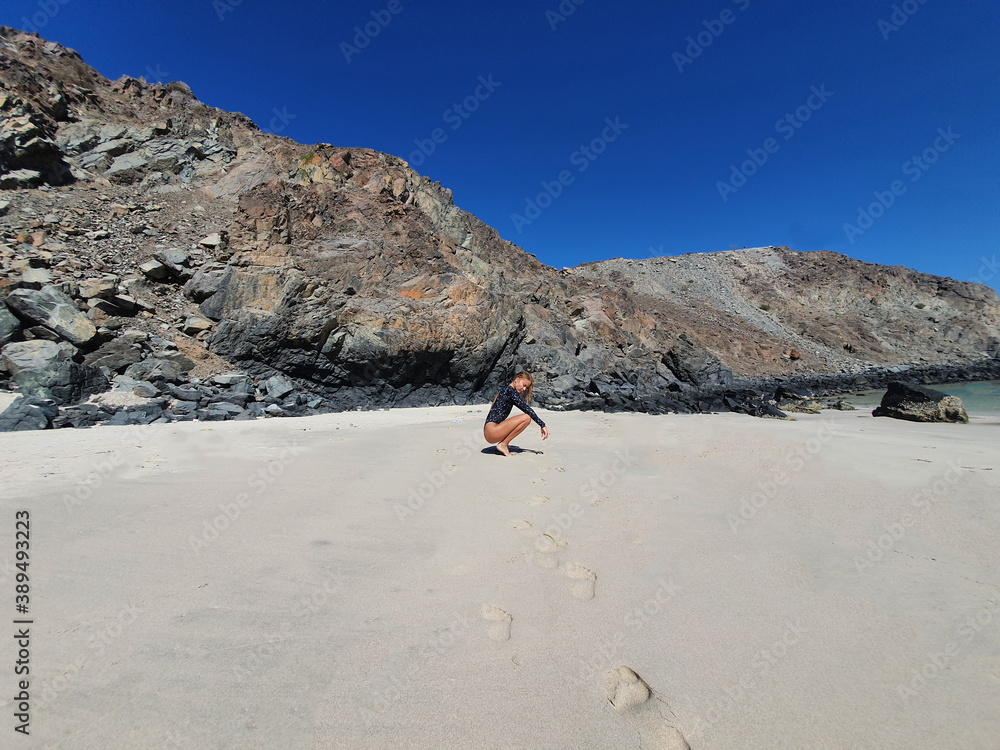 Woman sitting on the beach next to the rock