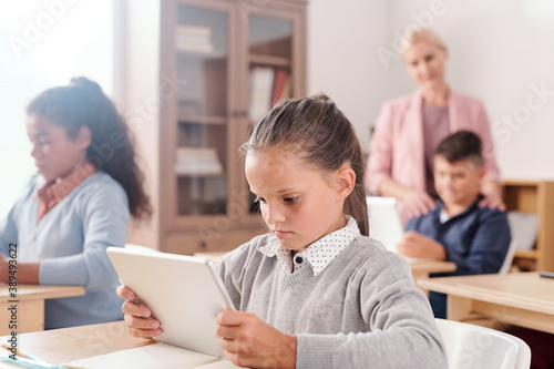 Cute girl and her classmates with tablets working individually with online text
