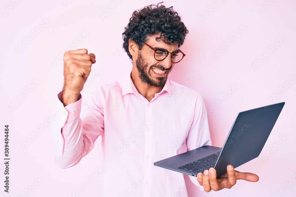 Handsome young man with curly hair and bear working using computer laptop annoyed and frustrated shouting with anger, yelling crazy with anger and hand raised Handsome young man with curly hair and bear working using computer laptop annoyed and frustrated shouting with anger, yelling crazy with anger and hand raised