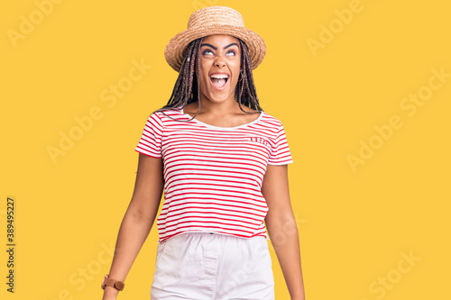 Young african american woman with braids wearing summer hat angry and mad screaming frustrated and furious, shouting with anger. rage and aggressive concept.
