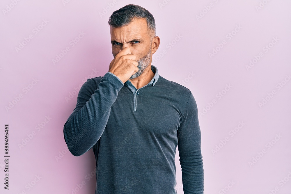 Middle age handsome man wearing casual clothes smelling something stinky and disgusting, intolerable smell, holding breath with fingers on nose. bad smell Middle age handsome man wearing casual clothes smelling something stinky and disgusting, intolerable smell, holding breath with fingers on nose. bad smell