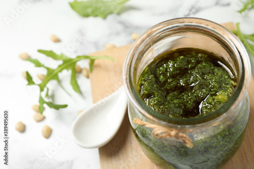 Jar of tasty arugula pesto on white table, closeup