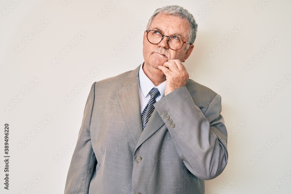 Senior grey-haired man wearing business suit thinking concentrated about doubt with finger on chin and looking up wondering Senior grey-haired man wearing business suit thinking concentrated about doubt with finger on chin and looking up wondering