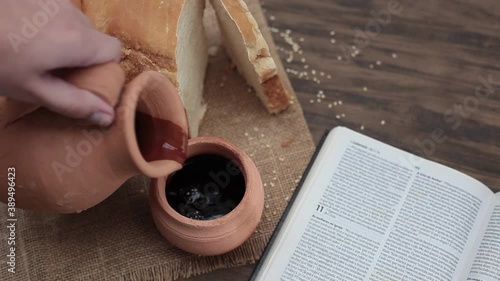 Bread, Bible and natural clay jug with wine being poured into a clay cup. Top view. Wood background. Celebration supper. Religion.