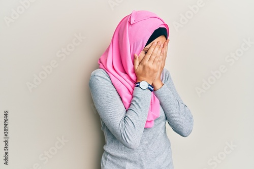 Young caucasian woman wearing traditional islamic hijab scarf with sad expression covering face with hands while crying. depression concept.