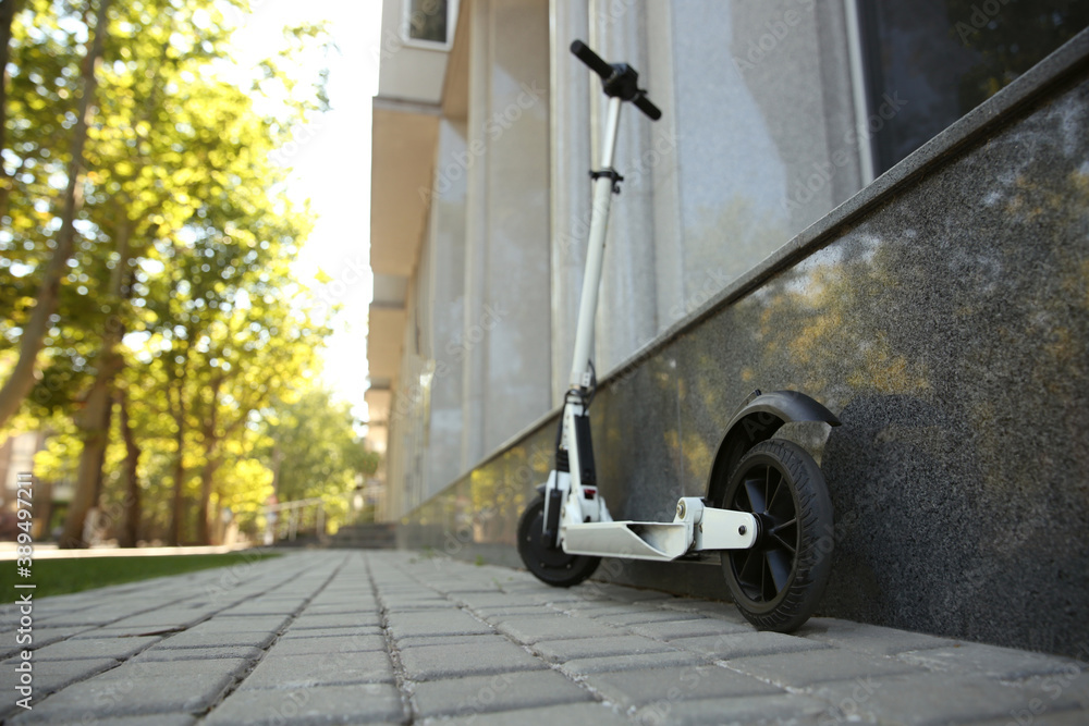 Fototapeta premium Modern electric kick scooter parked near building. Space for text