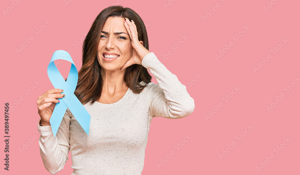 Young brunette woman holding blue ribbon stressed and frustrated with hand on head, surprised and angry face Young brunette woman holding blue ribbon stressed and frustrated with hand on head, surprised and angry face
