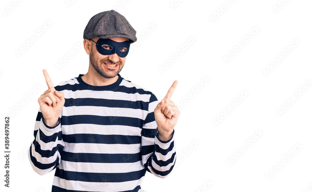 Young handsome man wearing burglar mask smiling confident pointing with fingers to different directions. copy space for advertisement Young handsome man wearing burglar mask smiling confident pointing with fingers to different directions. copy space for advertisement