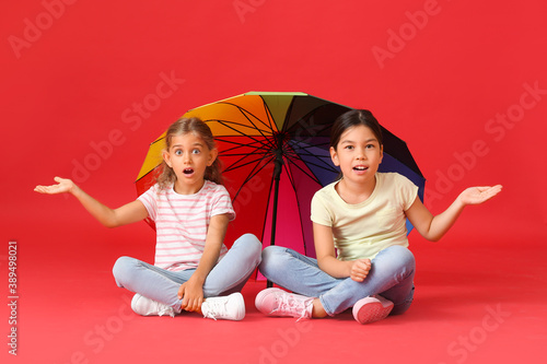 Surprised little girls with rainbow umbrella on color background