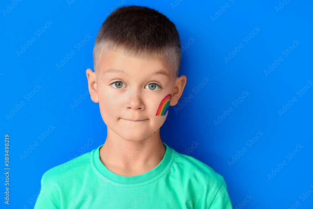 Little boy with painted rainbow on his face against color background Little boy with painted rainbow on his face against color background