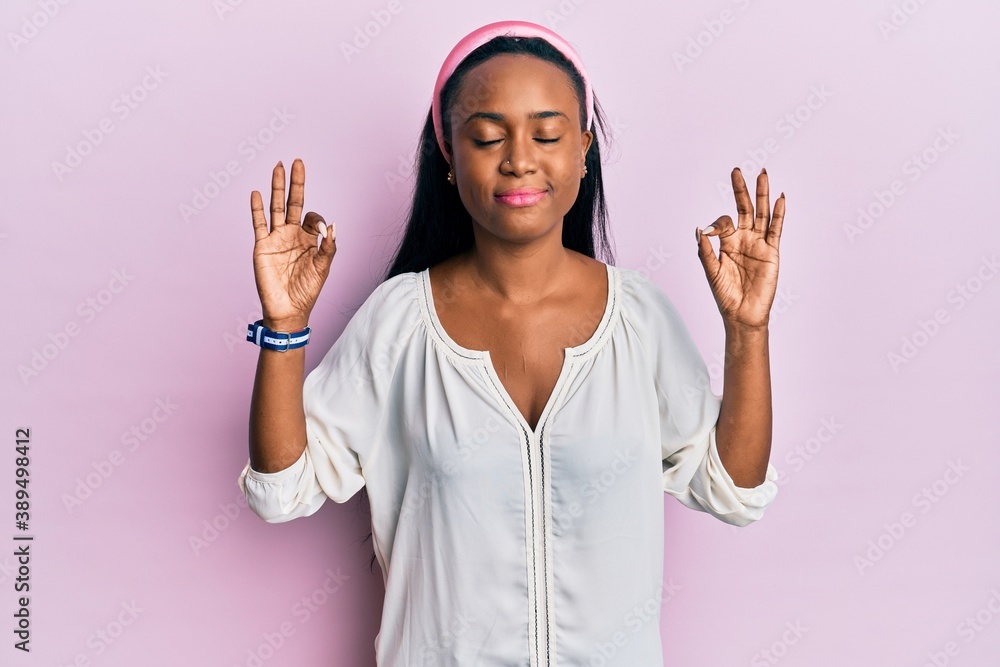 Young african woman wearing casual clothes over pink background relax and smiling with eyes closed doing meditation gesture with fingers. yoga concept. Young african woman wearing casual clothes over pink background relax and smiling with eyes closed doing meditation gesture with fingers. yoga concept.