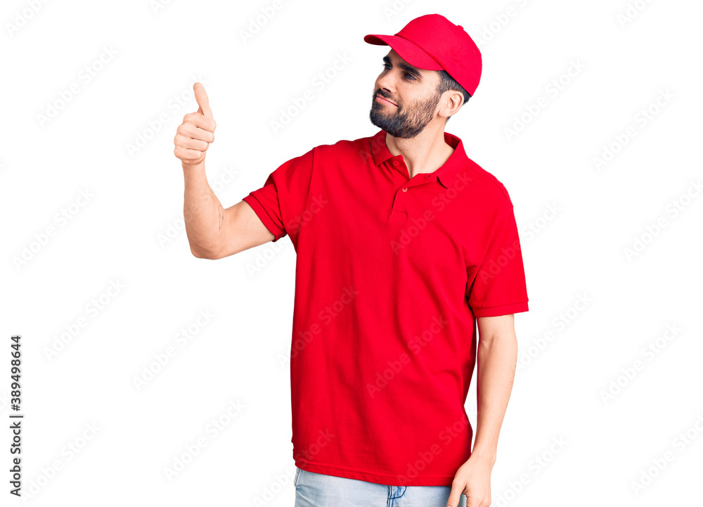 Young handsome man with beard wearing delivery uniform looking proud, smiling doing thumbs up gesture to the side Young handsome man with beard wearing delivery uniform looking proud, smiling doing thumbs up gesture to the side