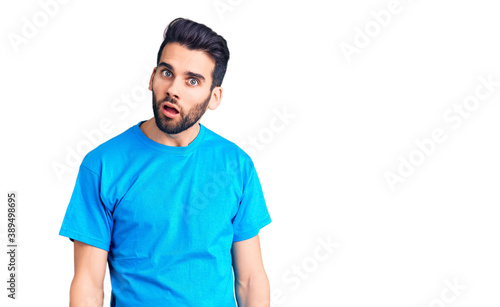 Young handsome man with beard wearing casual t-shirt in shock face, looking skeptical and sarcastic, surprised with open mouth