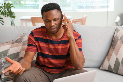 Stressed African-American man talking by phone at home © Pixel-Shot
