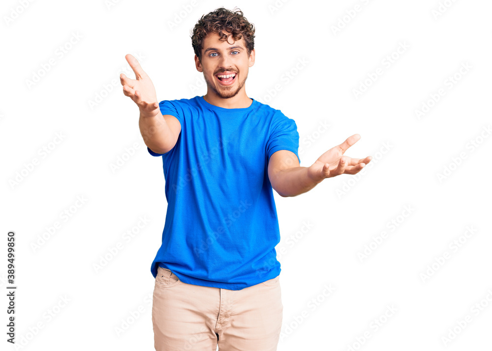Young handsome man with curly hair wearing casual clothes smiling cheerful offering hands giving assistance and acceptance. Young handsome man with curly hair wearing casual clothes smiling cheerful offering hands giving assistance and acceptance.