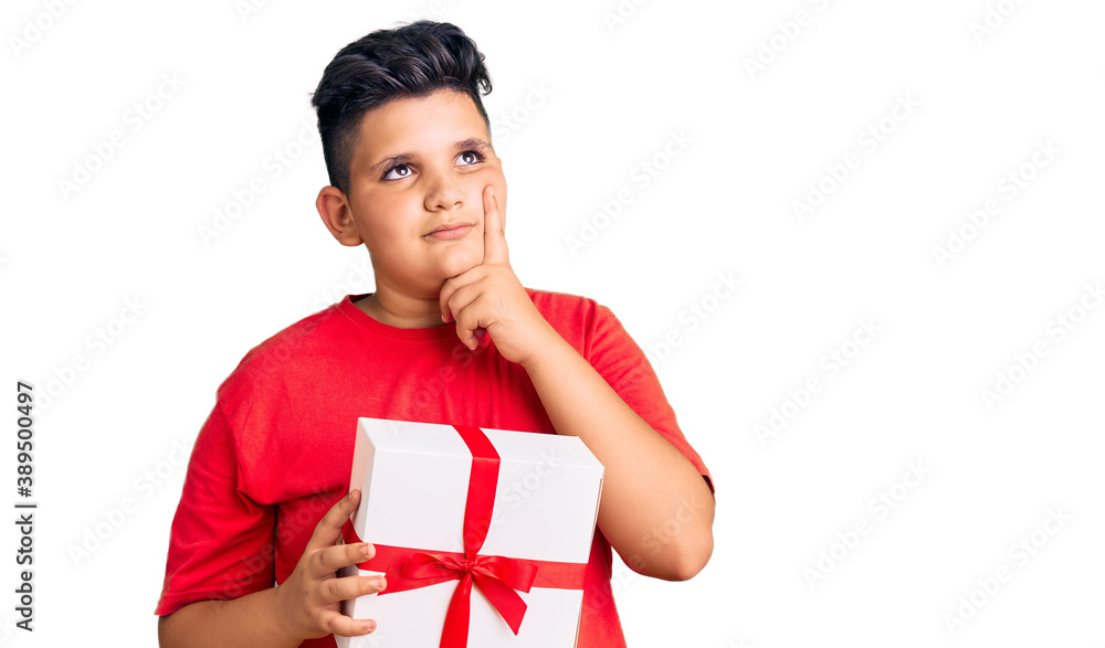 Little boy kid holding gift serious face thinking about question with hand on chin, thoughtful about confusing idea Little boy kid holding gift serious face thinking about question with hand on chin, thoughtful about confusing idea