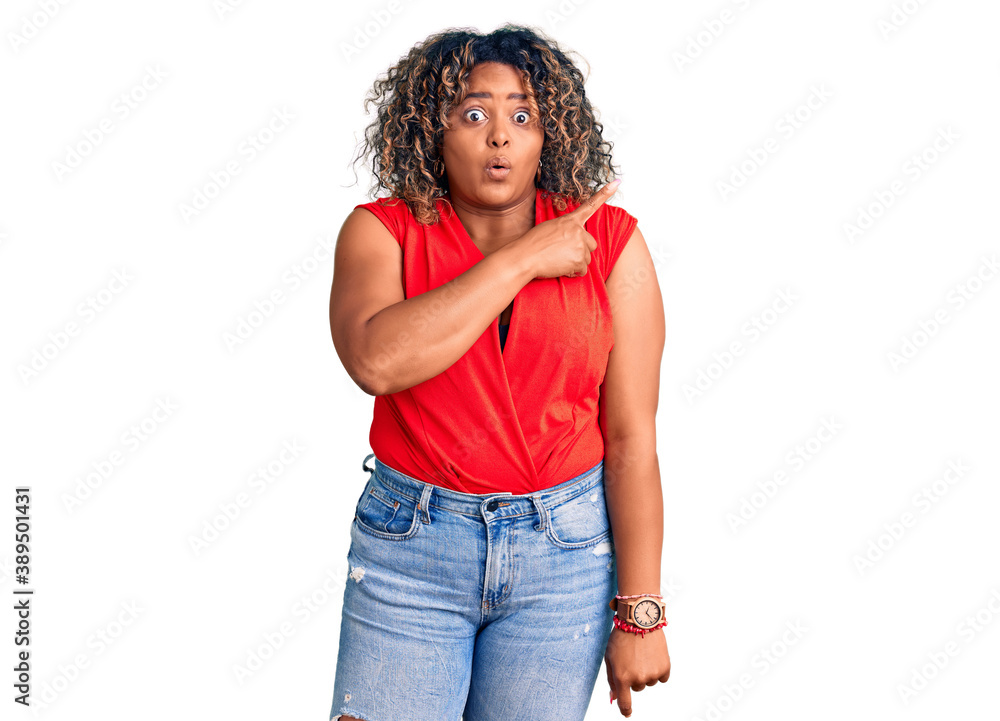 Young african american plus size woman wearing casual style with sleeveless shirt surprised pointing with finger to the side, open mouth amazed expression. Young african american plus size woman wearing casual style with sleeveless shirt surprised pointing with finger to the side, open mouth amazed expression.
