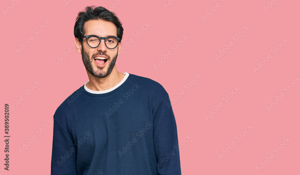 Young hispanic man wearing casual clothes and glasses winking looking at the camera with sexy expression, cheerful and happy face. Young hispanic man wearing casual clothes and glasses winking looking at the camera with sexy expression, cheerful and happy face.