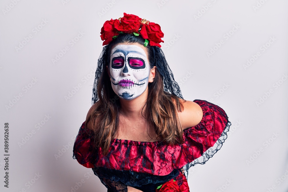 Young woman wearing day of the dead costume over white suffering of backache, touching back with hand, muscular pain