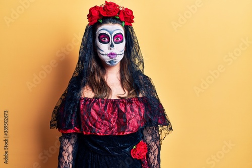 Young woman wearing day of the dead costume over yellow puffing cheeks with funny face. mouth inflated with air, crazy expression.