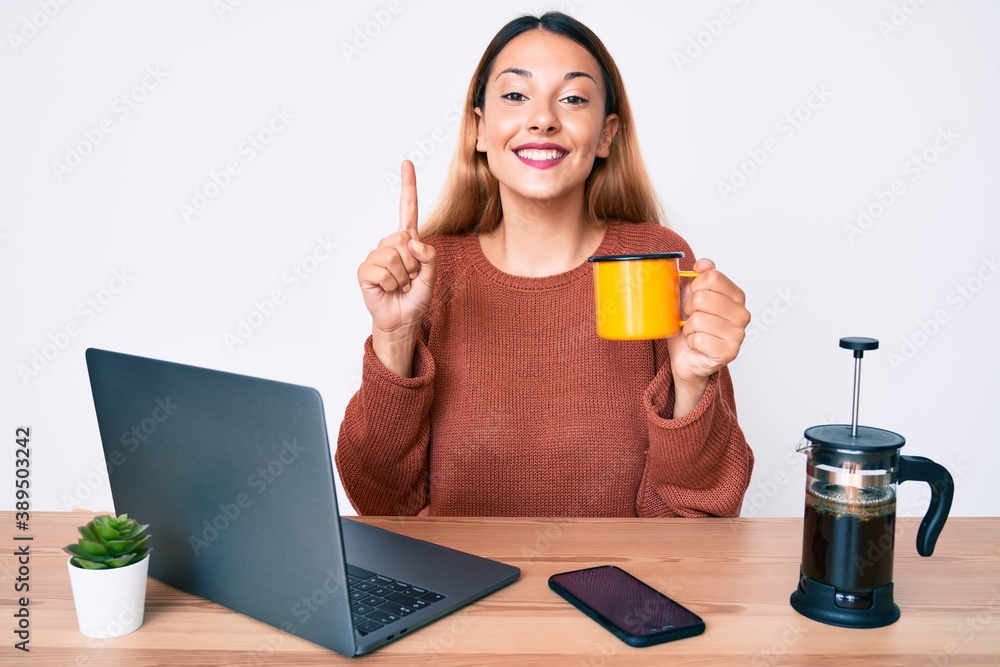 Young brunette woman working at the office drinking a cup of coffee smiling with an idea or question pointing finger with happy face, number one Young brunette woman working at the office drinking a cup of coffee smiling with an idea or question pointing finger with happy face, number one