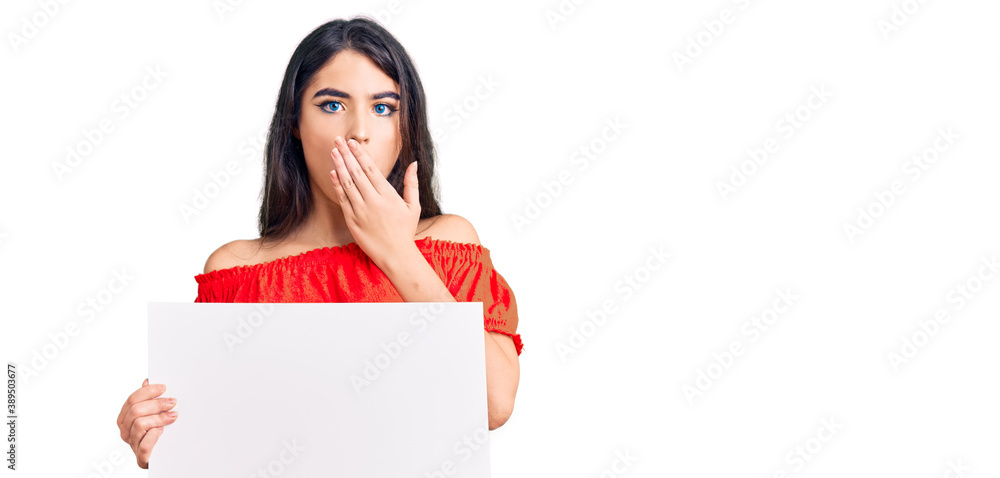Brunette teenager girl holding blank empty banner covering mouth with hand, shocked and afraid for mistake. surprised expression Brunette teenager girl holding blank empty banner covering mouth with hand, shocked and afraid for mistake. surprised expression