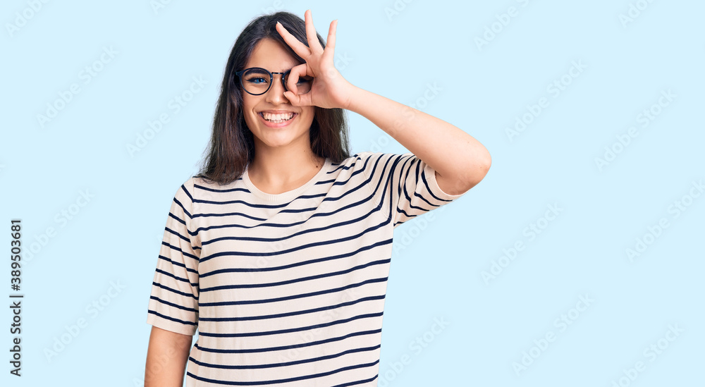 Brunette teenager girl wearing casual clothes and glasses doing ok gesture with hand smiling, eye looking through fingers with happy face.