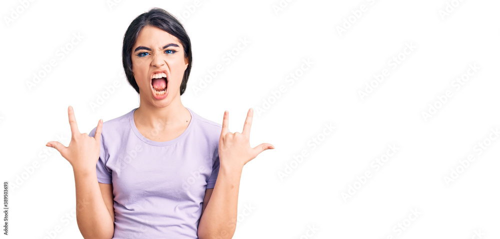 Brunette teenager girl wearing casual clothes shouting with crazy expression doing rock symbol with hands up. music star. heavy concept. Brunette teenager girl wearing casual clothes shouting with crazy expression doing rock symbol with hands up. music star. heavy concept.