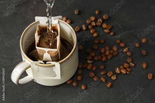 Pouring hot water into cup with drip coffee bag on black table, closeup