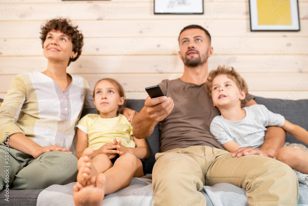 Hand of young serious man in casualwear pushing buttons of remote control Hand of young serious man in casualwear pushing buttons of remote control