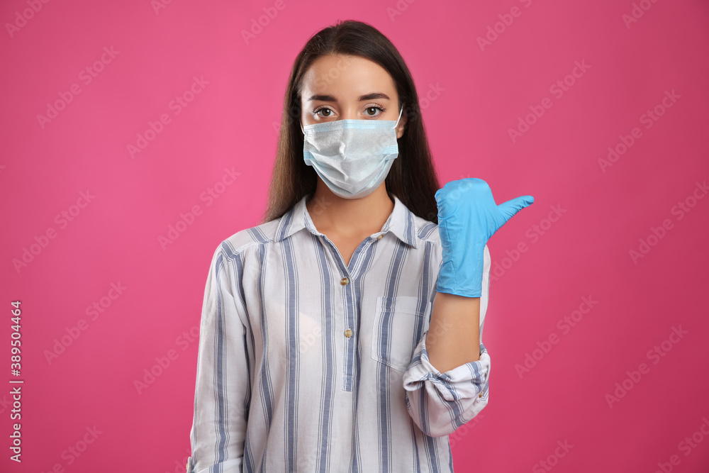 Woman in protective face mask and medical gloves pointing at something on pink background Woman in protective face mask and medical gloves pointing at something on pink background