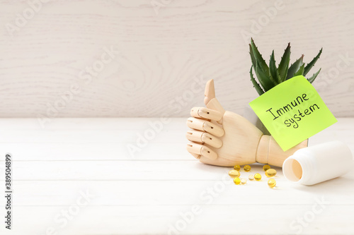 Mannequin hand, pills and note with phrase Immune System on white wooden table. Space for text photo