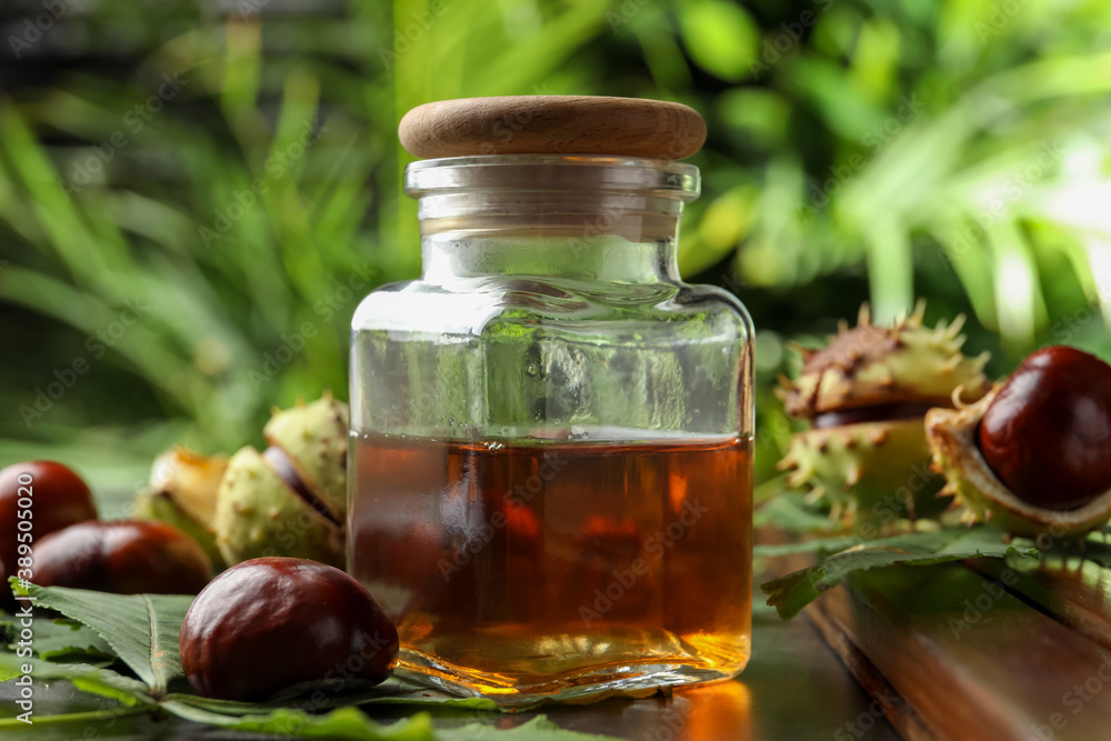 Chestnuts, leaves and jar of essential oil on table against blurred background Chestnuts, leaves and jar of essential oil on table against blurred background
