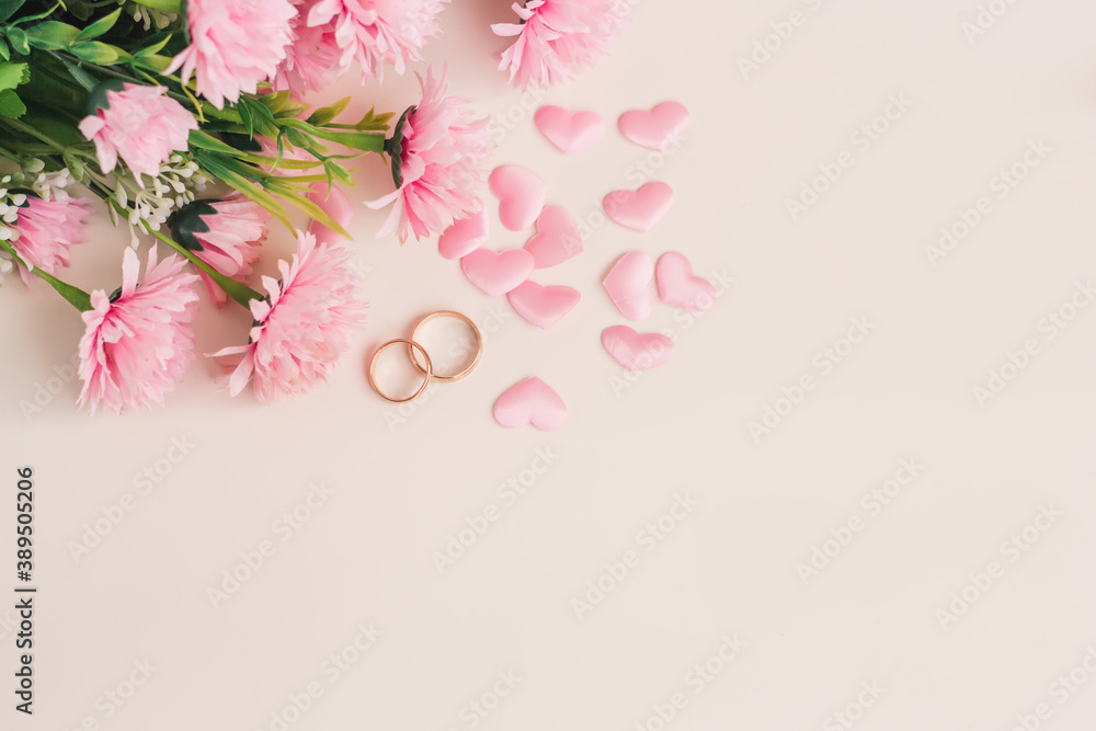 Fototapeta premium Pair of wedding rings surrounded by hearts and flowers. Top view with copy space