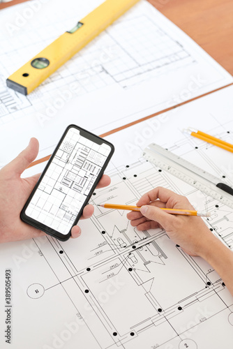 Hands of modern professional engineer or architect with pencil using smartphone