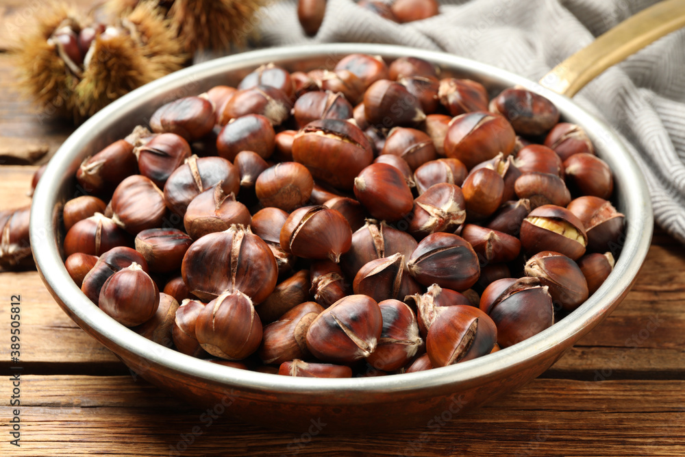 Delicious roasted edible chestnuts in frying pan on wooden table, closeup Delicious roasted edible chestnuts in frying pan on wooden table, closeup