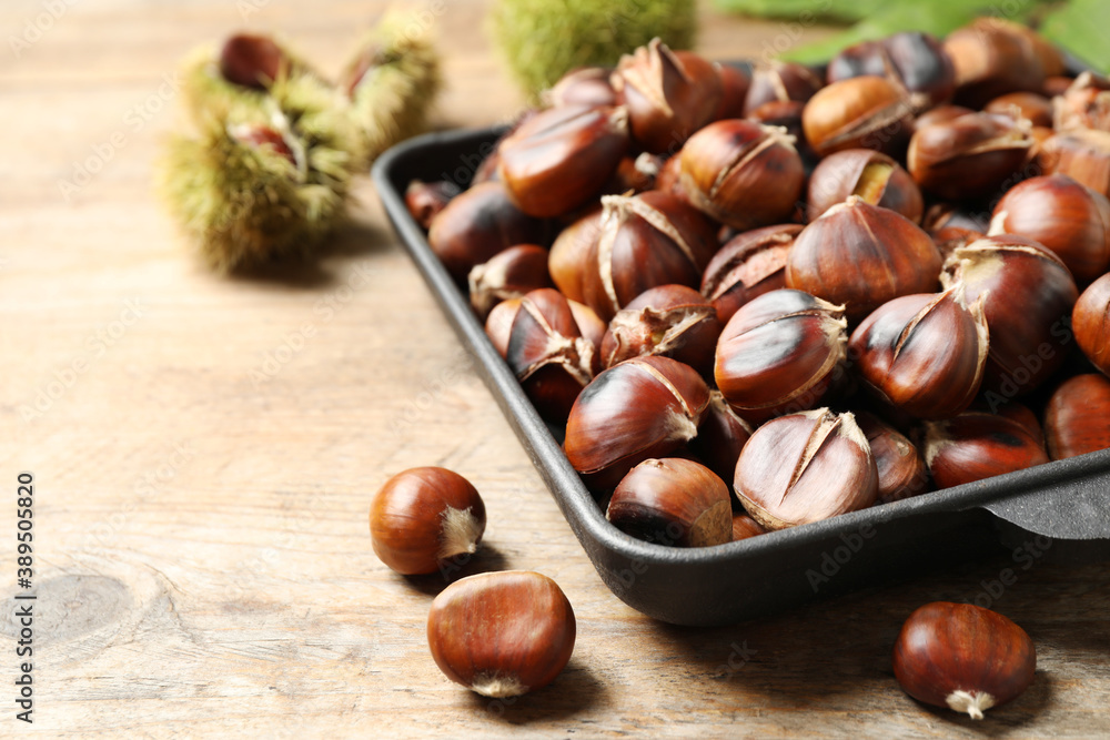 Delicious roasted edible chestnuts in baking dish on wooden table, closeup Delicious roasted edible chestnuts in baking dish on wooden table, closeup