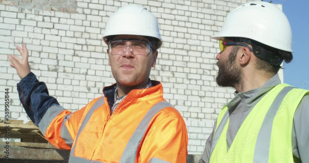 Builders discussing construction against brick wall Builders discussing construction against brick wall