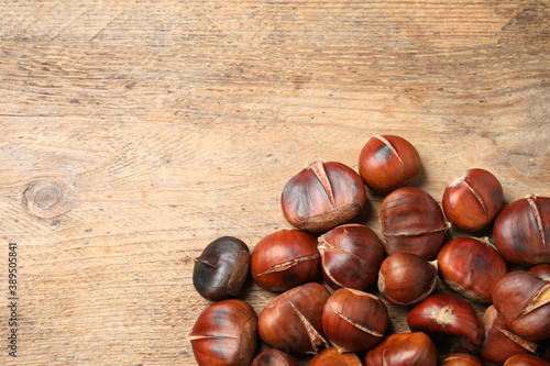 Delicious roasted edible chestnuts on wooden table, flat lay. Space for text