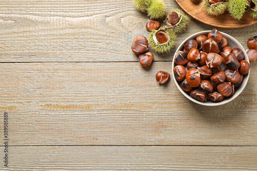 Delicious roasted edible chestnuts on wooden table, flat lay. Space for text