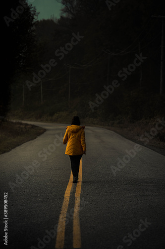 Woman in a yellow jacket walking on the road photo