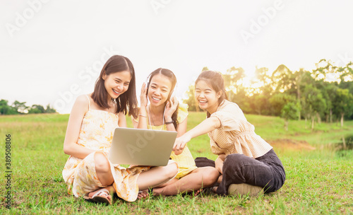 A group of young girls sitting on the meadow and used computers with wearing headphones. laughing and having fun on a relaxing day in summer.