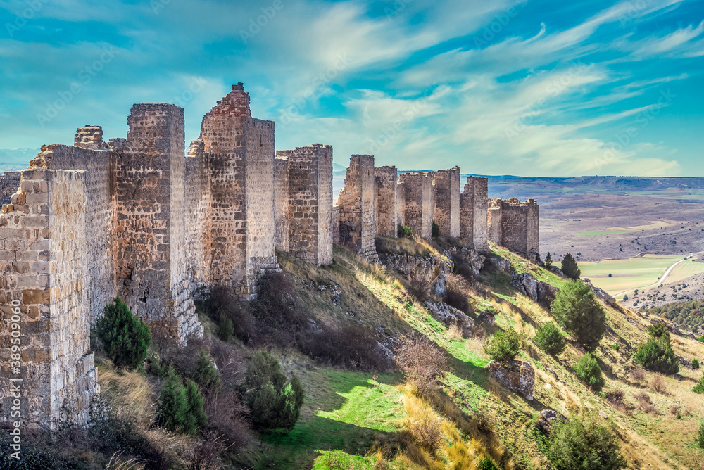Row of square towers projecting from the walls and casting shadow on the hill at medieval Gormaz castle in Spain with dreamy blue cloudy sky