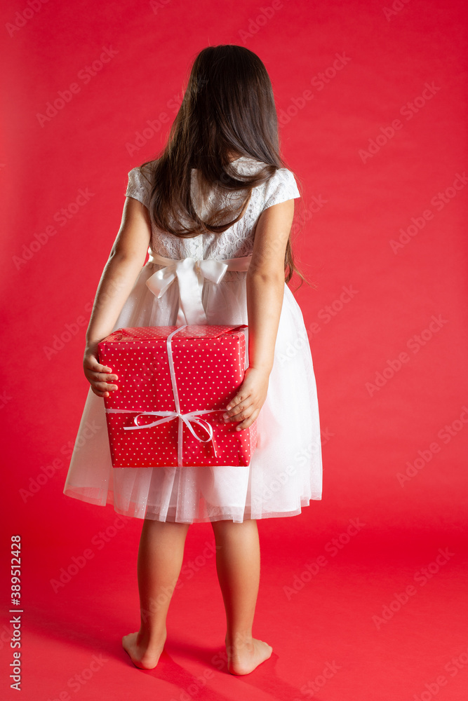 a full-length girl in a white dress stands with her back and holds a gift from behind, wants to give it to someone for Christmas or Valentine's day. a full-length girl in a white dress stands with her back and holds a gift from behind, wants to give it to someone for Christmas or Valentine's day.