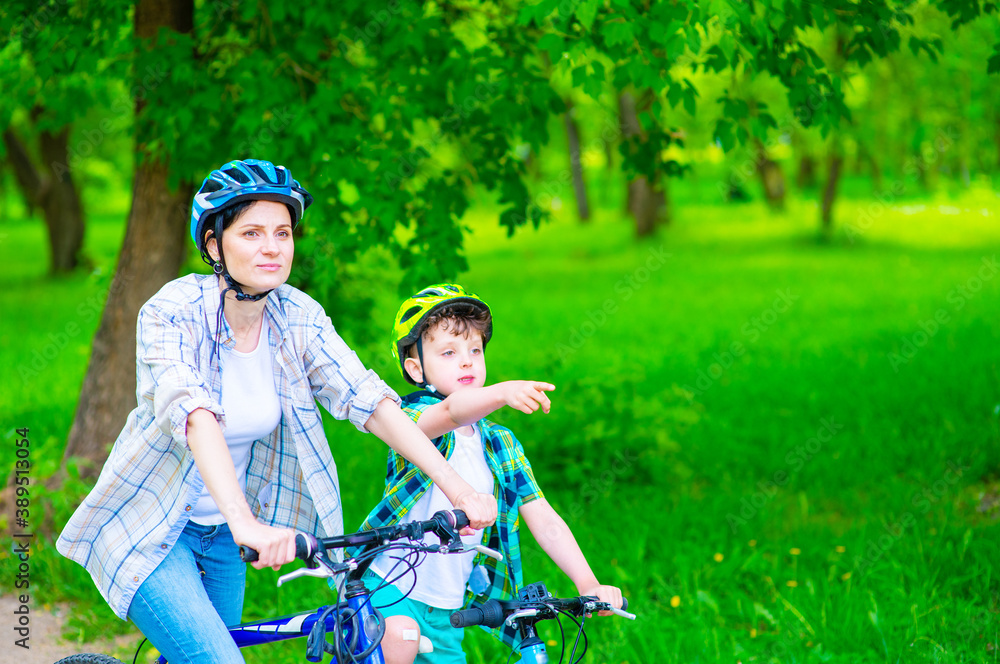 Mom and son riding bicycles in the park, son pointing in front of the movement with his forefinger. Family vacation concept