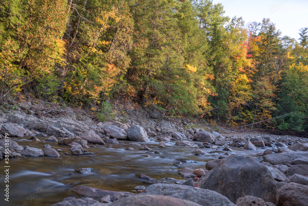 Long exposure of water flowing over rocks with fall foliage in the background Long exposure of water flowing over rocks with fall foliage in the background