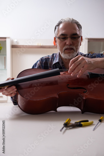 Obraz na plátně Senior male repairman repairing musical instruments at home