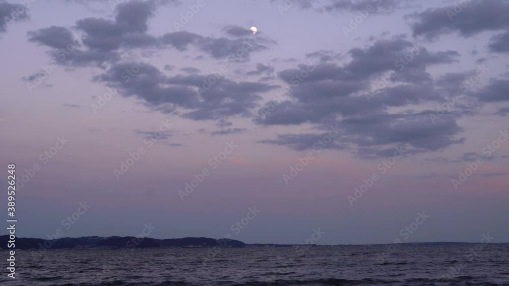 Beautiful view out on ocean at dusk with purple and pink colors and high above moon with moving clouds Beautiful view out on ocean at dusk with purple and pink colors and high above moon with moving clouds